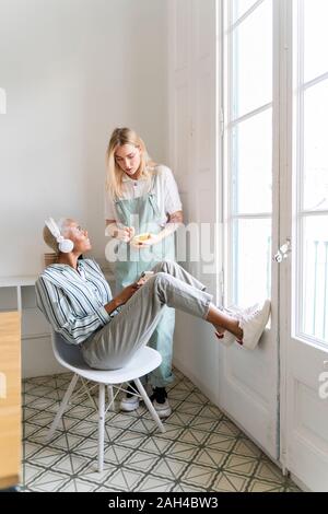 Zwei Frauen mit Kopfhörern und Handy am Fenster Stockfoto