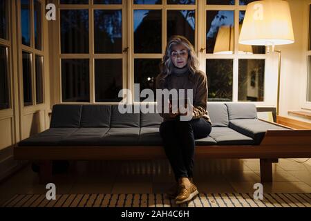 Reife Frau mit Tablet auf der Couch zu Hause in der Dunkelheit Stockfoto