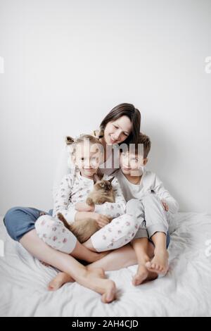 Mutter mit zwei Kindern und einer Katze sitzt auf dem Bett Stockfoto