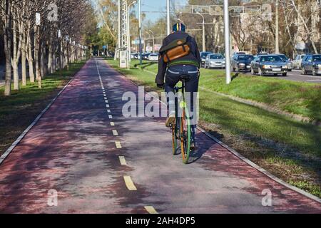 Ein Radfahrer in der Stadt bewegt sich ein Radweg. Umweltfreundliche Verkehrsträger. Ansicht von der Rückseite. Fahrrad mit fester Drehzahl Stockfoto