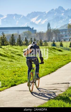 Ein Radfahrer fährt auf einer Straße in der Stadt vor dem Hintergrund des grünen Grases und die Berge. Stadt Almaty. Ökologische Verkehrspolitik. Stockfoto