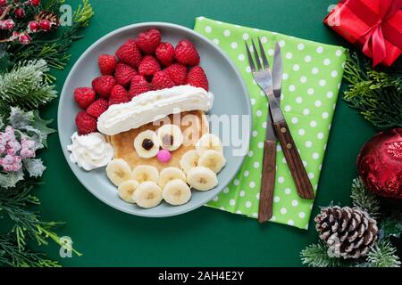 Winter Essen für Kinder. Weihnachten Santa Pfannkuchen mit Himbeeren und Banane für Kinder Menü, grüner Hintergrund, kopieren. Stockfoto