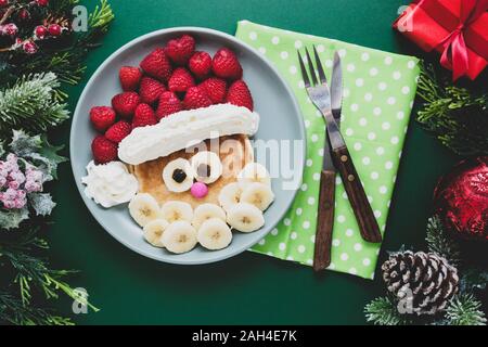 Winter Essen für Kinder. Weihnachten Santa Pfannkuchen mit Himbeeren und Banane für Kinder Menü, grüner Hintergrund, kopieren. Stockfoto