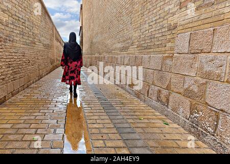 Einheimische Frau, die in der nassen Kopfsteinpflasterstraße, Shiraz, Iran, spazierengeht Stockfoto