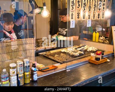 Eine Street Food vendor bereitet Austern zum Kochen mit frisch zubereiteten Austern zum Verkauf an einer auf der Insel Miyajima, Japan. Stockfoto