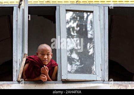 Junge Mönch Blick aus dem Fenster der Schlafsaal im Kloster, in Yangon, Myanmar Stockfoto