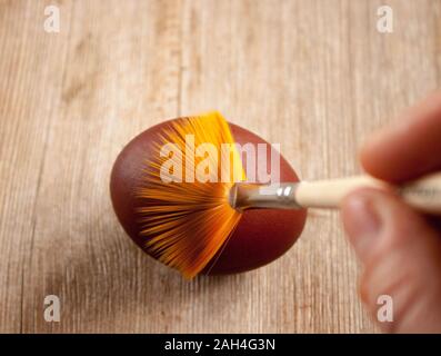 Menschliche Hand Malerei Osterei mit der Bürste. Top natürliche woodan Hintergrund anzeigen. Selektive Weichzeichner. Geringe Tiefenschärfe. Text kopieren. Ostern c Stockfoto