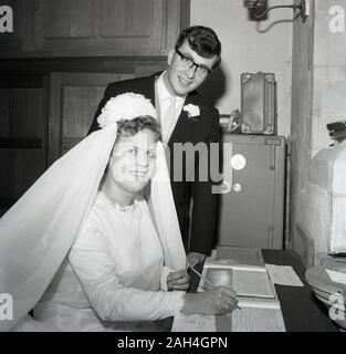 1960, historische, eine Braut und Bräutigam in einem Hinterzimmer einer Kirche, mit der Braut sitzen, die Unterzeichnung der Ehe registrieren, England, UK. Stockfoto