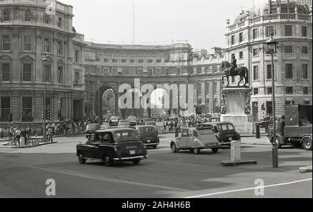 1970 s, historischen, London Taxis und Autos der Ära durch die Admiralty Arch, London, England. Im Auftrag von König Edward VII. dem Tod von Königin Victoria zum Gedenken an, und in Portland Stein gebaut und im Jahr 1912 abgeschlossen, der Bogen ist ein Wahrzeichen der Stadt, die Straße und Fußgänger zwischen den Trafalgar Square und die Mall, die bis auf die königliche Residenz führt, Buckingham Palace. Stockfoto