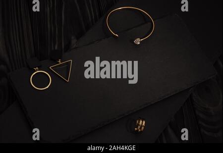 Goldenes Armband, Ring und geometrischen design Ohrringe auf dunklen Platten auf dunklem Hintergrund Stockfoto