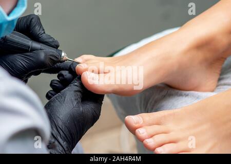 Pedicurist die Hände in Handschuhe mit Spezialwerkzeug, Pediküre der weiblichen Nägel auf die Füße. Fußpflege in Spa Salon, aus der Nähe. Stockfoto