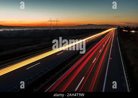 Autos leichte Wanderwege auf einer geraden Autobahn bei Sonnenuntergang. Traffic Night Trails, Bewegungsunschärfe, Nacht Stadt Straße mit verkehr Scheinwerfer Bewegung. Stockfoto