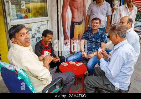 Lokale Männer spielen Karten auf dem Bürgersteig: Straßenszene in Mahipalpur Bezirk, einem Vorort in der Nähe von Delhi Flughafen in New Delhi, die Hauptstadt Indiens Stockfoto