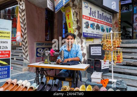 Straßenszene in Mahipalpur Bezirk, einem Vorort in der Nähe von Delhi Flughafen in New Delhi, die Hauptstadt Indiens: lokale Mann bei der Arbeit mit einem manuellen Nähmaschine Stockfoto