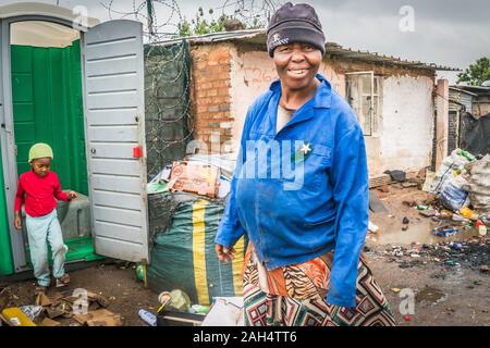 Johannesburg, Südafrika - Dezember 4, 2019 - Soweto Slums; Frau auf einer Straße; Kinder mit öffentlichen Toiletten; regnerischen Tag Stockfoto