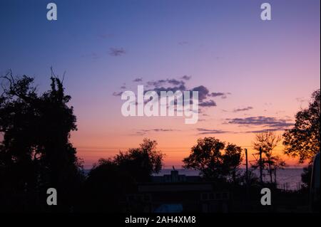 Sonnenuntergang über dem Meer mit Blick auf einen rosa Himmel mit lila Wolken und Bäumen. Subtropen, Sommer, Hitze, Erholung, Urlaub, Entspannung, Abend, Nacht. Stockfoto