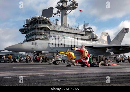 USS Abraham Lincoln in den Vereinigten Staaten. 24. Dezember, 2019. Ein U.S. Navy Matrose verkleidet als Weihnachtsmann leitet die Einführung eines F/A-18F Super Hornet Kampfflugzeuge auf dem Flugdeck der Nimitz-Klasse Flugzeugträger USS Abraham Lincoln bei Arbeiten an Heiligabend Dezember 24, 2019 in das Südchinesische Meer. Credit: Jeremia Bartelt/U.S. Marine/Alamy leben Nachrichten Stockfoto