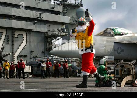 USS Abraham Lincoln in den Vereinigten Staaten. 24. Dezember, 2019. Ein U.S. Navy Matrose verkleidet als Weihnachtsmann leitet die Einführung eines F/A-18E Super Hornet Kampfflugzeuge auf dem Flugdeck der Nimitz-Klasse Flugzeugträger USS Abraham Lincoln bei Arbeiten an Heiligabend Dezember 24, 2019 in das Südchinesische Meer. Credit: Jeremia Bartelt/U.S. Marine/Alamy leben Nachrichten Stockfoto