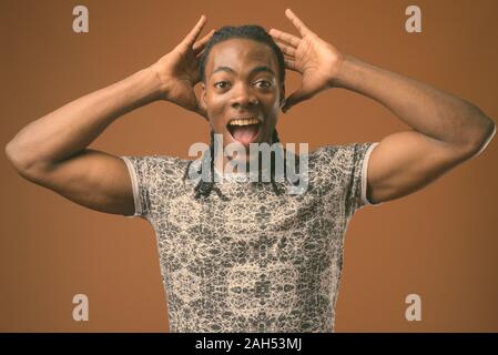 Studio shot der jungen schönen afrikanischen Mann mit grauen Hemd gegen braunen Hintergrund Stockfoto