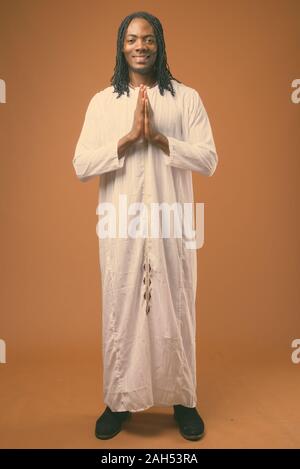 Studio shot der jungen schönen afrikanischen Mann in traditioneller Kleidung vor braunen Hintergrund Stockfoto