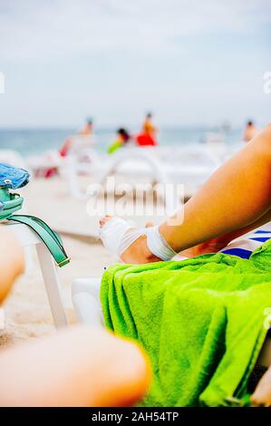 Mullbinde die Behandlung von Patienten mit Mann wickelt seine Fußverletzung am Strand Stockfoto