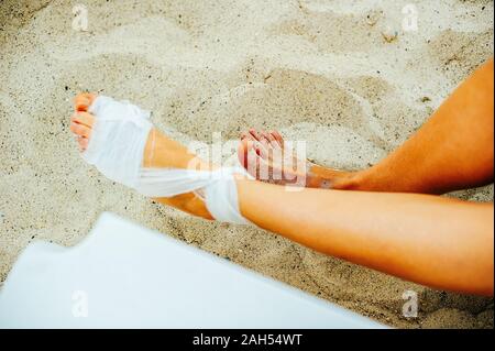 Mullbinde die Behandlung von Patienten mit Mann wickelt seine Fußverletzung am Strand Stockfoto