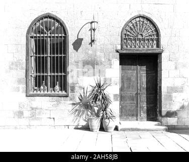 Schwarze und weiße hoher Kontrast von alten Stein Ziegel Wand mit gewölbten Tür und Fenster bedeckt mit schmiedeeisernen Bars und Laterne an einem sonnigen Tag, Kairo, Ägypten Stockfoto