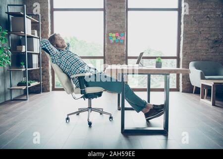 Full Body Profil Seite Foto von freudiger, Freelancer mit blonden Haaren in Stuhl Träumen tragen karierte Plaid Shirt Hose im Innenraum Stockfoto