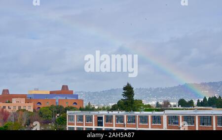 Rainbow über Emeryville über dem Sherwin-Williams-Lager und dem ehemaligen Novartis Gebäude oder dem "Emeryville Center of Innovation". Berkeley Hills dahinter. Stockfoto