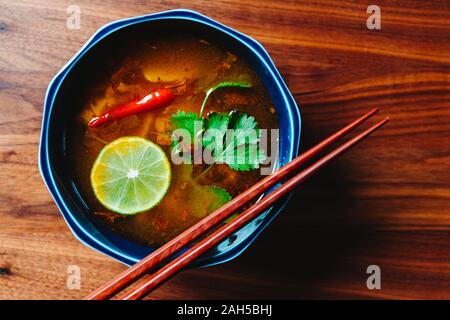 Blick von oben auf die vegetarische Thai Tom Yum Suppe mit Pilzen auf einem Holztisch. Stockfoto