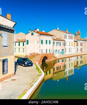 Eine Straße der kleinen italienischen Stadt Comacchio. Farbige Häuser im Wasser spiegelt. Brücke aus Stein und Wasser Kanal im Venezianischen Stil. Stockfoto