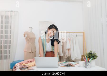 Fashion Trends zu diskutieren. Schöne junge Frau spricht auf dem Mobiltelefon und Arbeiten am Laptop beim Stehen in Ihrem Workshop Stockfoto