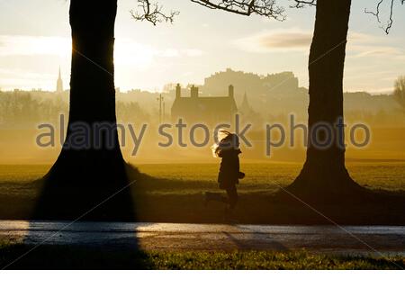 Edinburgh, Schottland, Großbritannien. 25. Dez 2019. Kalt, klar und hell mit geringer Masse Nebel am Weihnachtstag bei Sonnenaufgang in Inverleith Park, mit Blick auf das Edinburgh Castle. Kind im Park läuft. Quelle: Craig Brown/Alamy leben Nachrichten Stockfoto