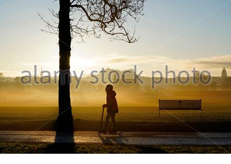 Edinburgh, Schottland, Großbritannien. 25. Dez 2019. Kalt, klar und hell mit geringer Masse Nebel am Weihnachtstag bei Sonnenaufgang in Inverleith Park, mit Blick auf das Edinburgh Castle. Kind auf dem Motorroller. Quelle: Craig Brown/Alamy leben Nachrichten Stockfoto