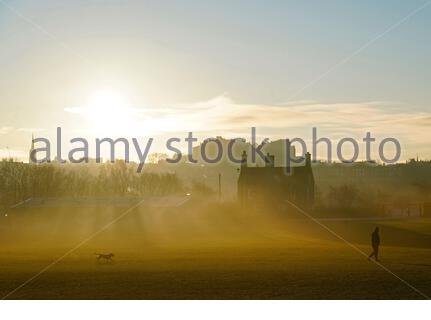 Edinburgh, Schottland, Großbritannien. 25. Dez 2019. Kalt, klar und hell mit geringer Masse Nebel am Weihnachtstag bei Sonnenaufgang in Inverleith Park, mit Blick auf das Edinburgh Castle. Mann mit seinem Hund. Quelle: Craig Brown/Alamy leben Nachrichten Stockfoto