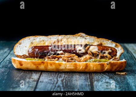 Hot Dog mit karamellisierten Zwiebeln, Cheddar und Greyerzer Käse Soße auf Holz- Oberfläche mit Kartoffeln. Fast Food. Stockfoto