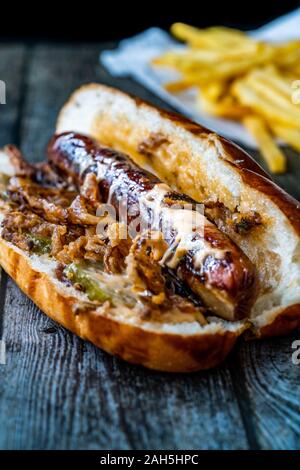 Hot Dog mit karamellisierten Zwiebeln, Cheddar und Greyerzer Käse Soße auf Holz- Oberfläche mit Kartoffeln. Fast Food. Stockfoto