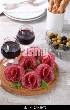 Leichte Mahlzeit Snack von Salami in der Form einer Blume mit einem Glas Sherry auf eine hölzerne Schüssel gefaltet. Stockfoto