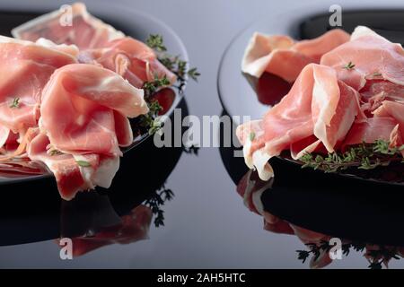 Prosciutto mit Thymian auf schwarzem Teller. Schwarz reflektierenden Hintergrund. Stockfoto