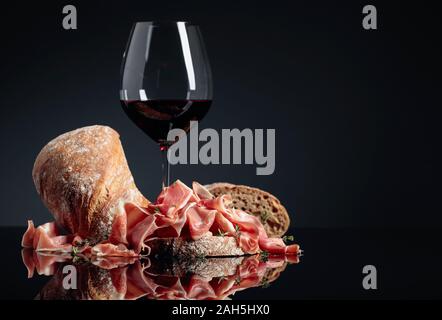 Prosciutto mit Ciabatta, Rotwein und Thymian auf ein schwarzes reflektierenden Hintergrund. Kopieren Sie Platz. Stockfoto