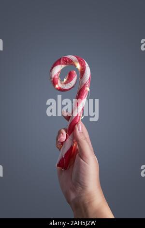 Seltsamerweise curly Zuckerstange mit LED-Leuchte in der Hand der Frauen gegen den grauen Hintergrund. Vertikales Format mit Platz kopieren Stockfoto