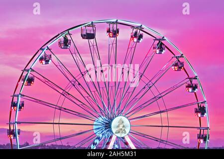 Closeup bunten Riesenrad gegen Sonnenuntergang rosa Himmel. Abstrakte Stadtbild Blick, Bewegungsunschärfe, selektiven Fokus Stockfoto