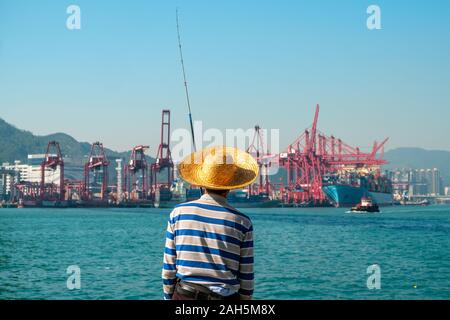 Fisher Mann mit Angelrute von hinten in der Nähe der Container schiff und Fracht Hafen in HongKong Stockfoto