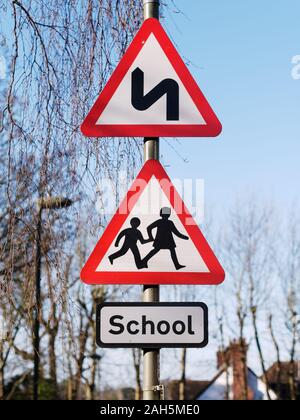 Doppel erste Biegung nach links Zeichen und Schule Kinder Kreuzung unterzeichnen. UK Straßenverkehr dreieckiges Warnzeichen Stockfoto