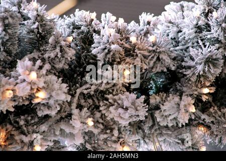 Traditionelle Weihnachten blinkende Lichter auf grüne Zweige Baum der Kiefer mit Schnee im Winter abgedeckt. Tannenbaum Äste mit string Reis Glühlampen. Stockfoto