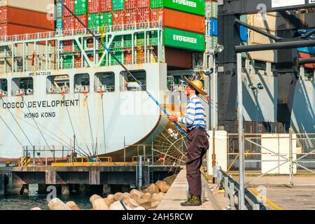 Fisher Mann mit Angelrute von hinten in der Nähe der Container schiff und Fracht Hafen in HongKong Stockfoto