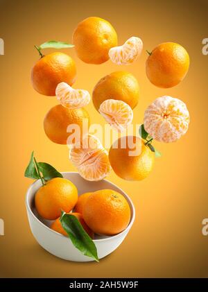 Tangerinen fliegen über orange Hintergrund, in eine Schüssel von unten isoliert, frische, saisonale Tangerinen Stockfoto