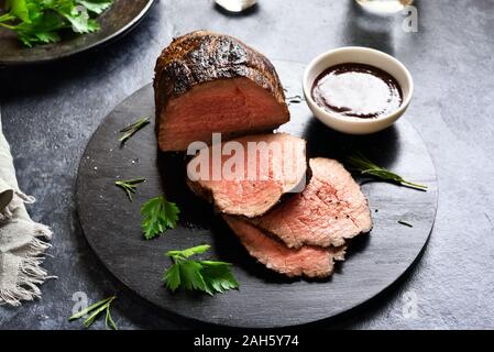 In Scheiben geschnitten gegrilltes Rindfleisch auf Holzbrett über dunklen Stein Hintergrund. Stockfoto