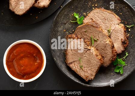 In Scheiben geschnitten Gegrilltes Roastbeef mit Tomatensauce auf dem schwarzen Stein. Ansicht von oben, flach Stockfoto
