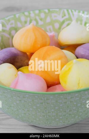 Baisers, verschiedene Farben, in einem grün gemusterten Schüssel Schüssel. Graues Holz Hintergrund Stockfoto